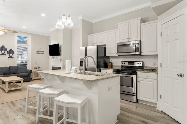 kitchen featuring ornamental molding, appliances with stainless steel finishes, light wood finished floors, and a sink