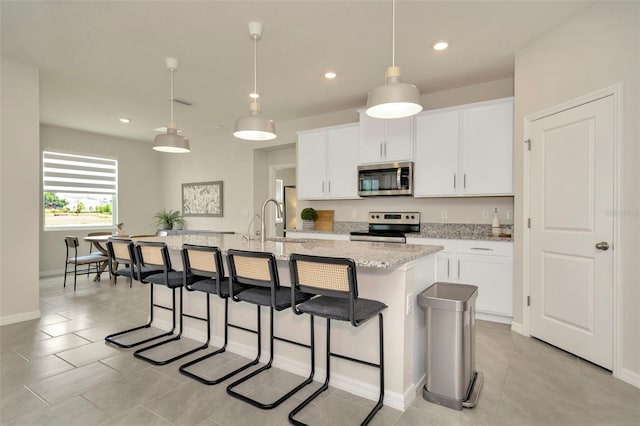 3504 Golden Wheat Ln, Plant City, FL 33565 - kitchen featuring stainless steel appliances, a center island with sink, light tile patterned floors, a kitchen breakfast bar, and white cabinetry