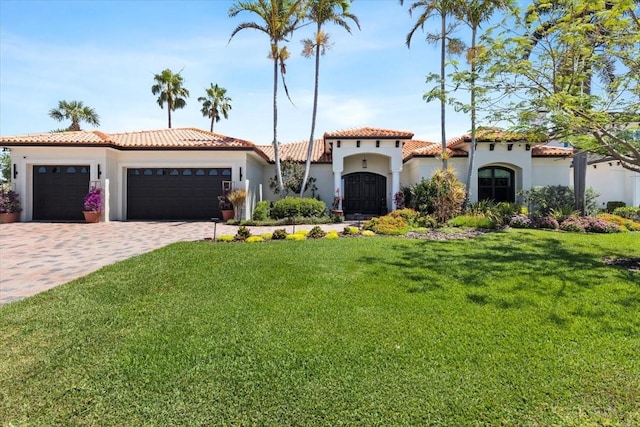 mediterranean / spanish house featuring an attached garage, a tiled roof, a front lawn, and stucco siding