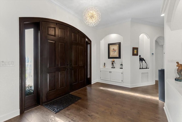 entryway with arched walkways, dark wood finished floors, visible vents, an inviting chandelier, and ornamental molding