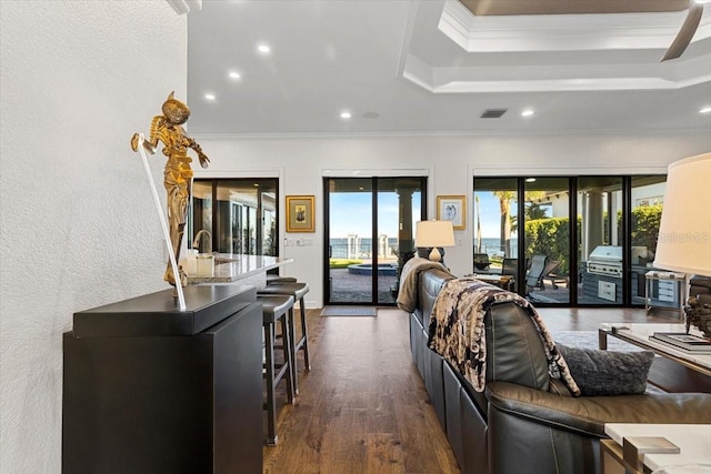 living area with a raised ceiling, ornamental molding, dark wood-type flooring, visible vents, and recessed lighting