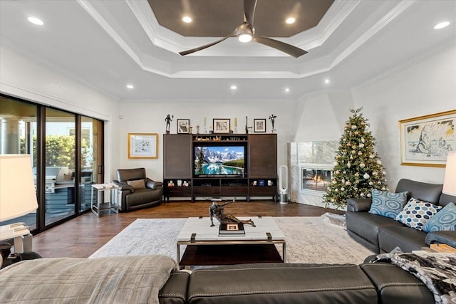 living room with a tray ceiling, wood finished floors, a ceiling fan, ornamental molding, and a premium fireplace