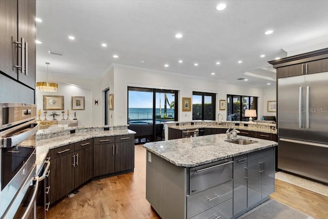 kitchen featuring a peninsula, a warming drawer, stainless steel built in fridge, crown molding, and an island with sink