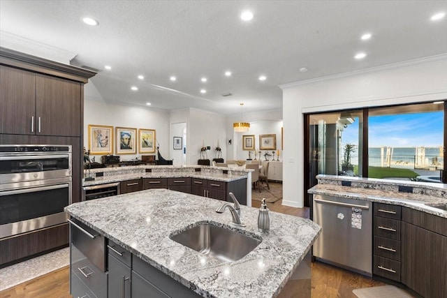 kitchen featuring a kitchen island with sink, a sink, dark brown cabinetry, crown molding, and appliances with stainless steel finishes