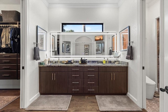 bathroom featuring double vanity, a spacious closet, wood finished floors, crown molding, and a textured wall