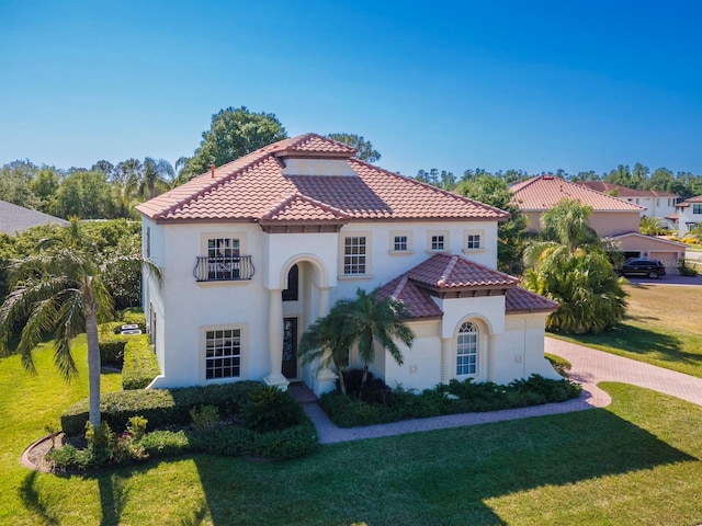 mediterranean / spanish-style home featuring a front lawn, stucco siding, a tiled roof, and a balcony