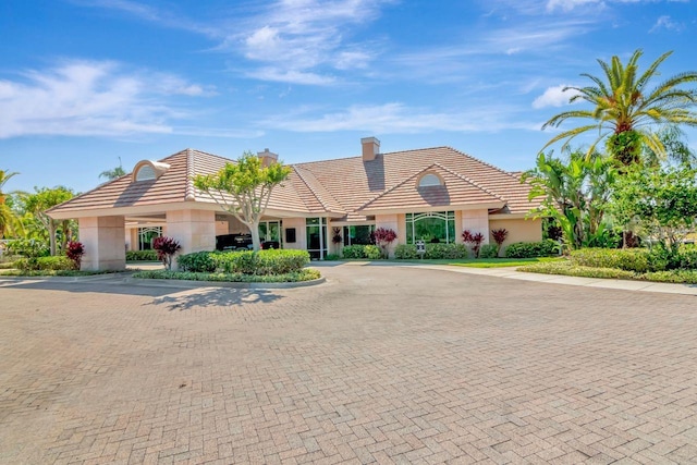 view of front of property featuring curved driveway, stucco siding, a tiled roof, and a chimney