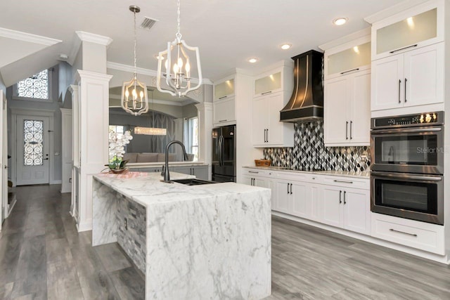 kitchen with a sink, black appliances, ornamental molding, custom exhaust hood, and a notable chandelier