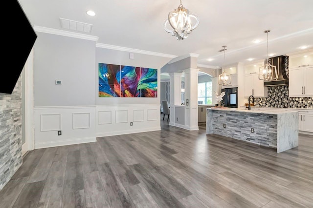 unfurnished living room featuring a sink, an inviting chandelier, decorative columns, visible vents, and arched walkways