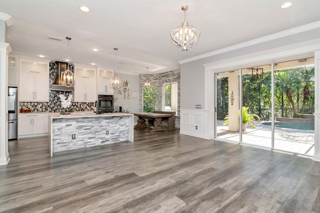 kitchen featuring a chandelier, backsplash, wall chimney range hood, white cabinets, and dobule oven black