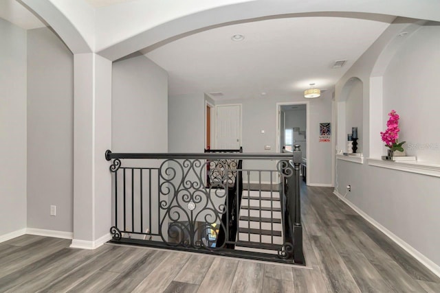 hall featuring baseboards, visible vents, wood finished floors, and arched walkways