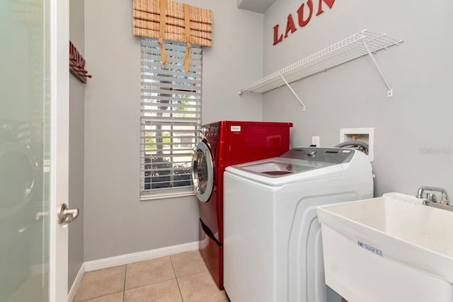 clothes washing area with light tile patterned floors, a sink, washing machine and dryer, baseboards, and laundry area