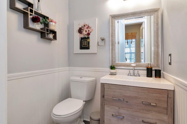 half bathroom featuring a wainscoted wall, toilet, and vanity