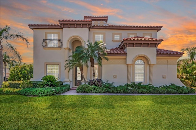 mediterranean / spanish-style house featuring a lawn, stucco siding, a tiled roof, and a balcony