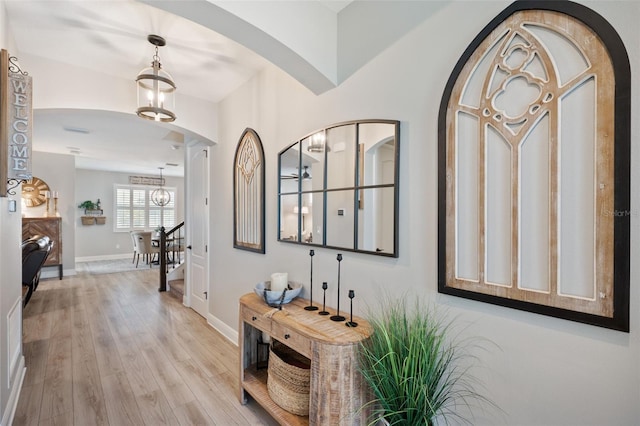 entrance foyer with arched walkways, light wood-style floors, and baseboards