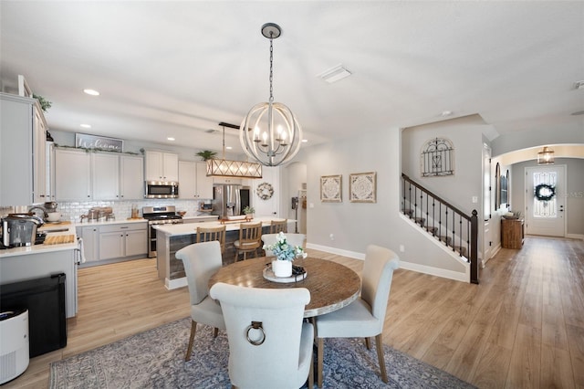 dining room featuring arched walkways, baseboards, an inviting chandelier, light wood-style floors, and stairway