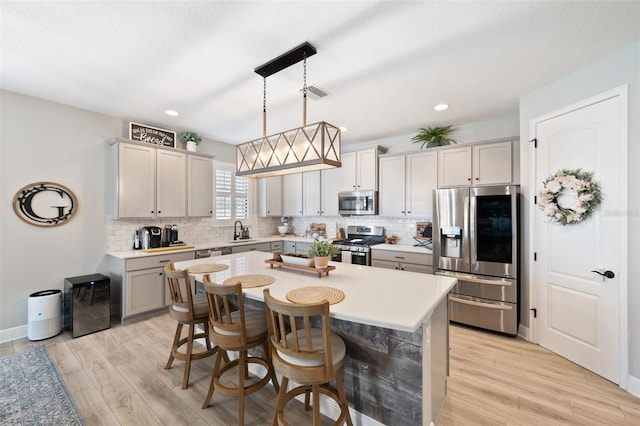 kitchen featuring a sink, light wood-type flooring, visible vents, decorative backsplash, and appliances with stainless steel finishes