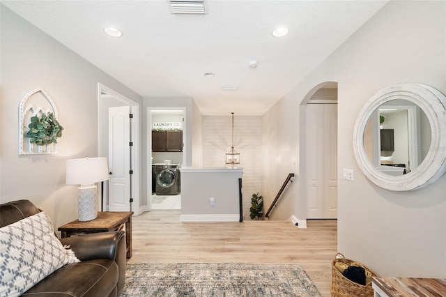hall featuring an upstairs landing, washer / dryer, light wood finished floors, baseboards, and visible vents