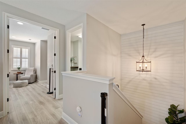 hallway with visible vents, an inviting chandelier, baseboards, light wood-style floors, and an upstairs landing