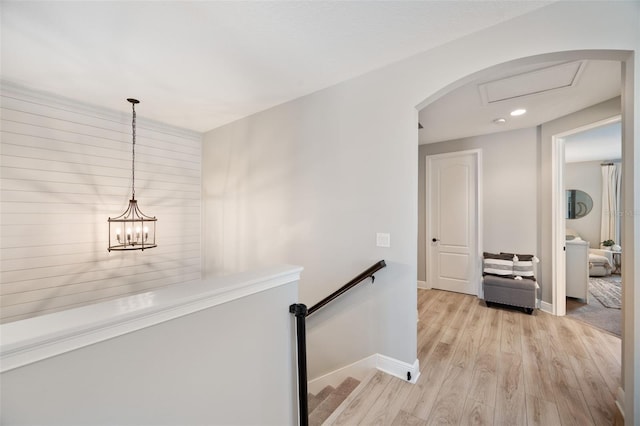 hallway with arched walkways, light wood-style floors, baseboards, and an upstairs landing