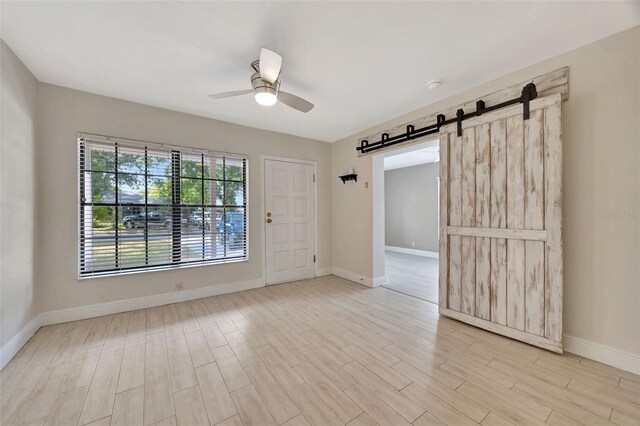 unfurnished room featuring a barn door, baseboards, light wood-style floors, and ceiling fan