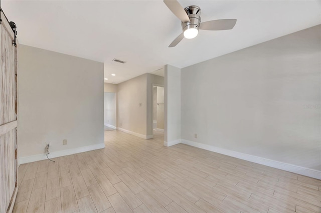 empty room featuring a barn door, light wood-type flooring, baseboards, visible vents, and a ceiling fan