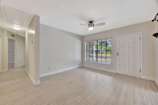 unfurnished room with attic access, light wood-style floors, a ceiling fan, and baseboards