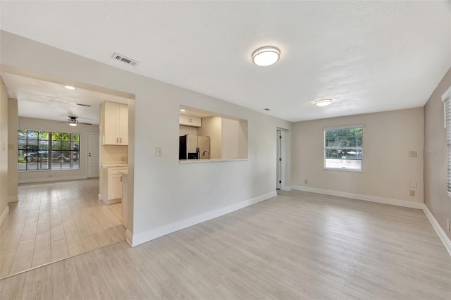 unfurnished living room with light wood-type flooring, baseboards, a ceiling fan, and visible vents