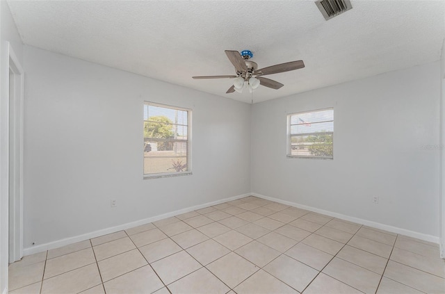 empty room featuring light tile patterned floors, a ceiling fan, visible vents, and baseboards