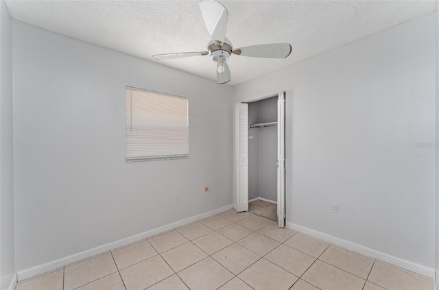 unfurnished bedroom with a closet, ceiling fan, baseboards, a textured ceiling, and light tile patterned flooring