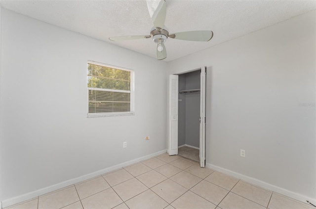 unfurnished bedroom featuring a closet, baseboards, a ceiling fan, a textured ceiling, and light tile patterned flooring
