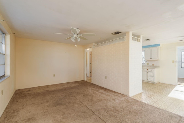 spare room with visible vents, ceiling fan, and light carpet