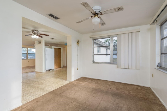 carpeted spare room featuring baseboards, a wealth of natural light, a ceiling fan, and visible vents