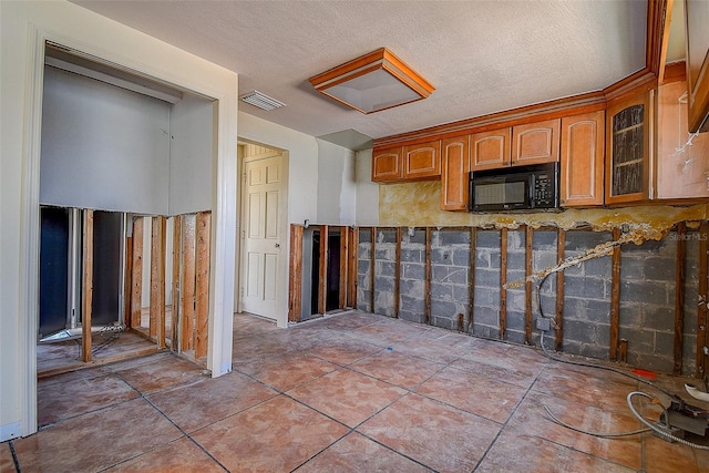kitchen featuring black microwave, a textured ceiling, brown cabinetry, visible vents, and glass insert cabinets