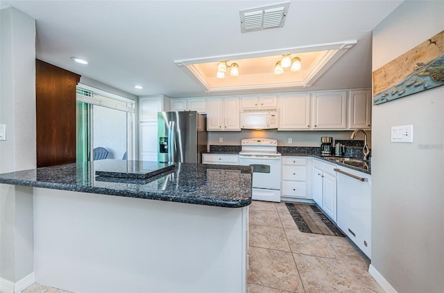 kitchen with a peninsula, a tray ceiling, a sink, visible vents, and white appliances