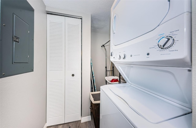 laundry area featuring electric panel, baseboards, wood finished floors, stacked washer / drying machine, and laundry area