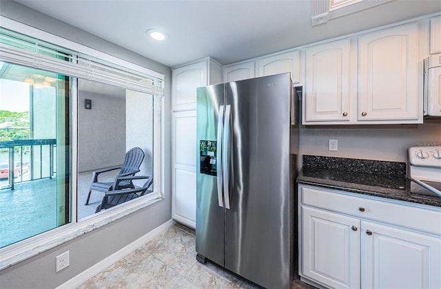 kitchen featuring dark stone counters, stainless steel refrigerator with ice dispenser, white cabinetry, and baseboards
