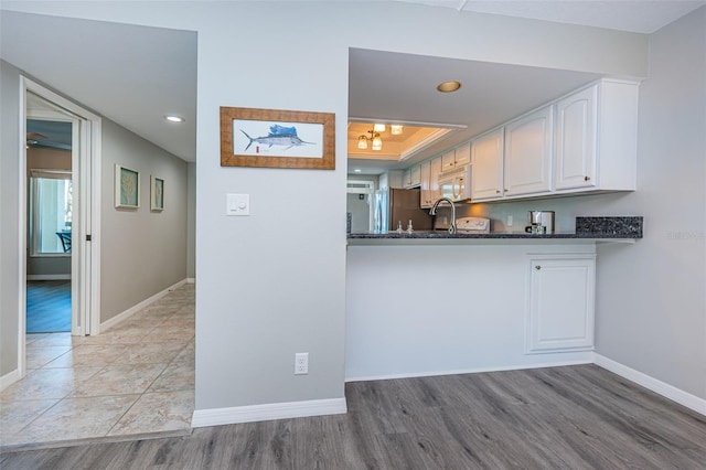 kitchen featuring white cabinets, light wood finished floors, a tray ceiling, baseboards, and white microwave