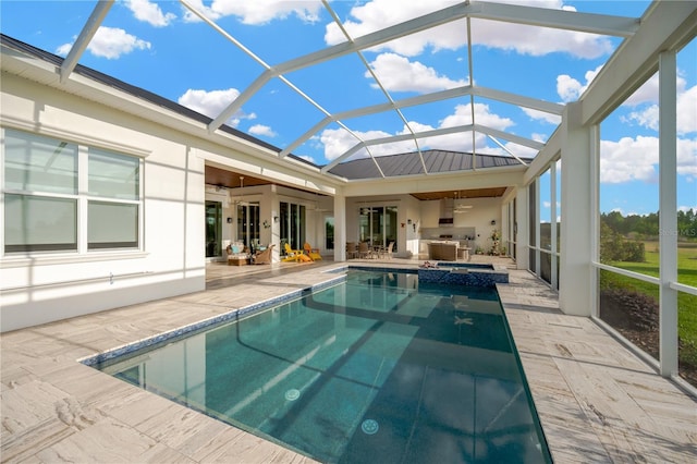 view of swimming pool with a pool with connected hot tub, an outdoor kitchen, ceiling fan, a patio, and glass enclosure