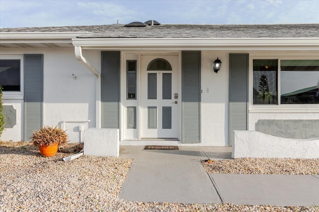 view of exterior entry with a porch, a shingled roof, and stucco siding