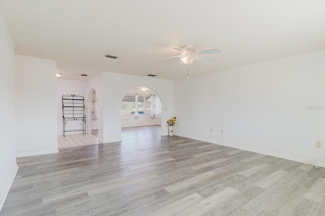 spare room with arched walkways, ceiling fan, light wood-style flooring, and visible vents