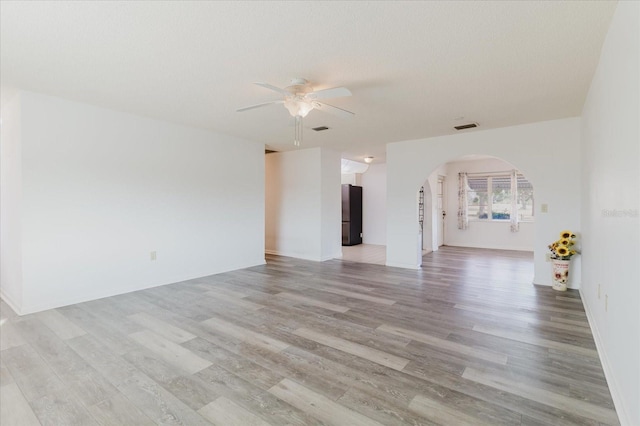 unfurnished room featuring visible vents, arched walkways, light wood-style flooring, and ceiling fan