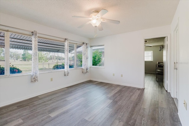 spare room with a textured ceiling, ceiling fan, baseboards, and wood finished floors