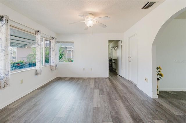 empty room with arched walkways, a ceiling fan, baseboards, wood finished floors, and visible vents