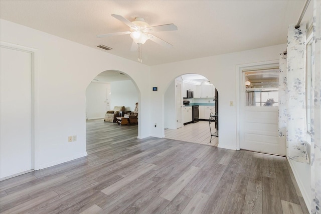 spare room featuring a ceiling fan, visible vents, arched walkways, baseboards, and light wood-style floors