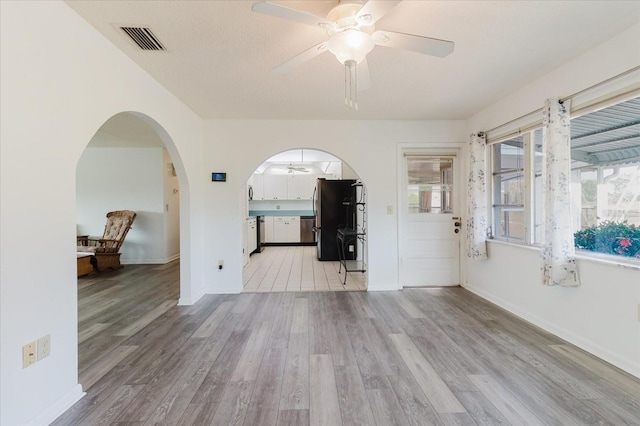 interior space with visible vents, baseboards, ceiling fan, arched walkways, and light wood-style flooring