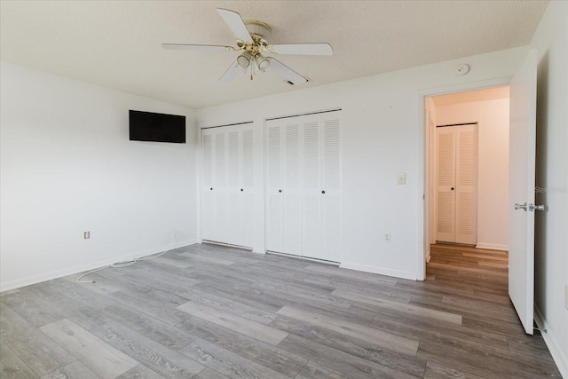unfurnished bedroom with two closets, a ceiling fan, baseboards, and wood finished floors