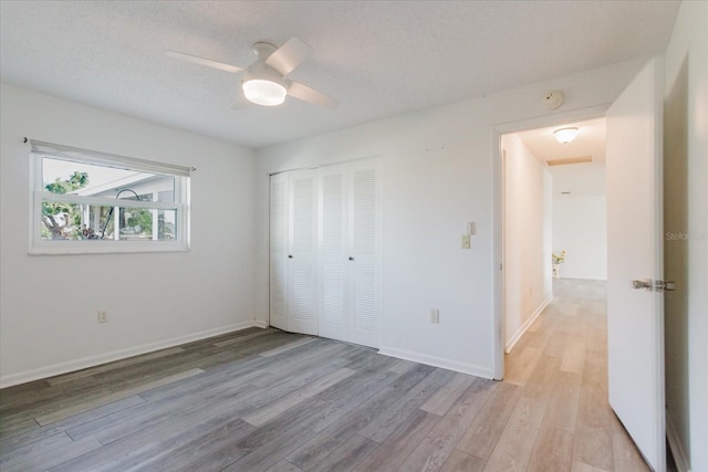 unfurnished bedroom with a closet, light wood-style flooring, ceiling fan, and baseboards