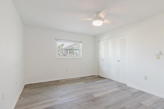 unfurnished bedroom featuring baseboards, ceiling fan, a closet, and light wood-style flooring