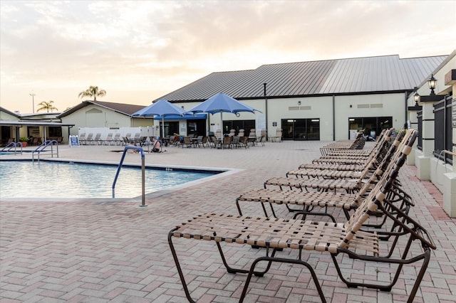 pool at dusk featuring a patio, a community pool, and fence
